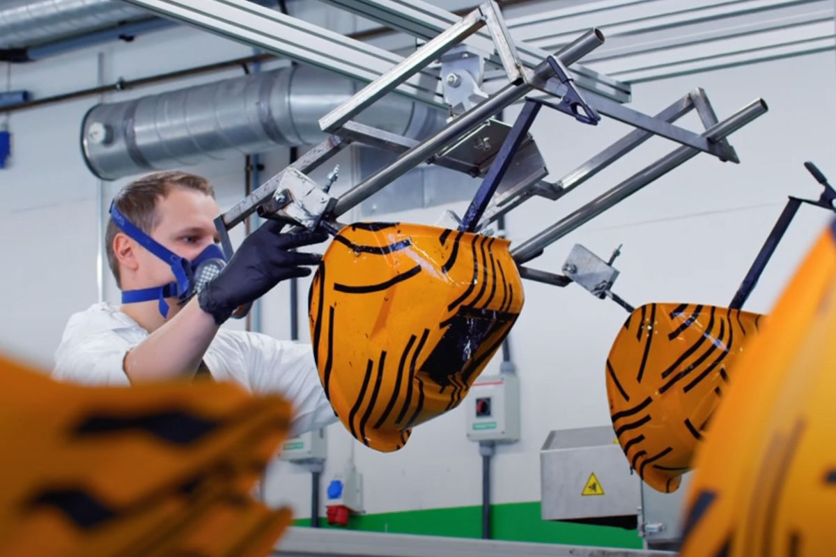 Valkoisiin pukeutunut miesoletettu asettelee oranssia ja raitakuvioista hitsauskypärää water printing -linjastolle.